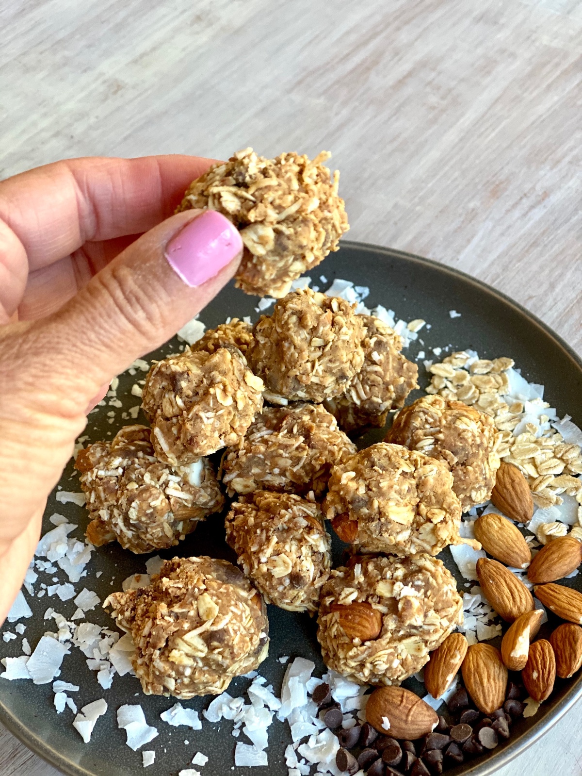 Hand holding coconut energy balls above plate of energy bites.